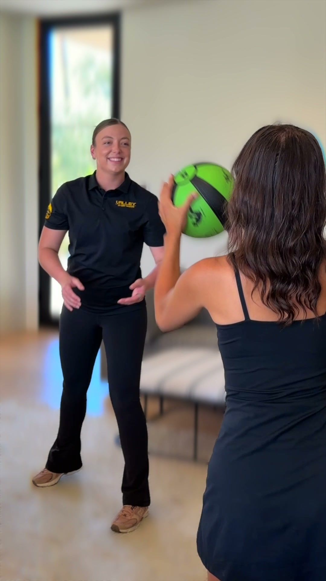 Trainer passing a medicine ball to a client in a bright living room