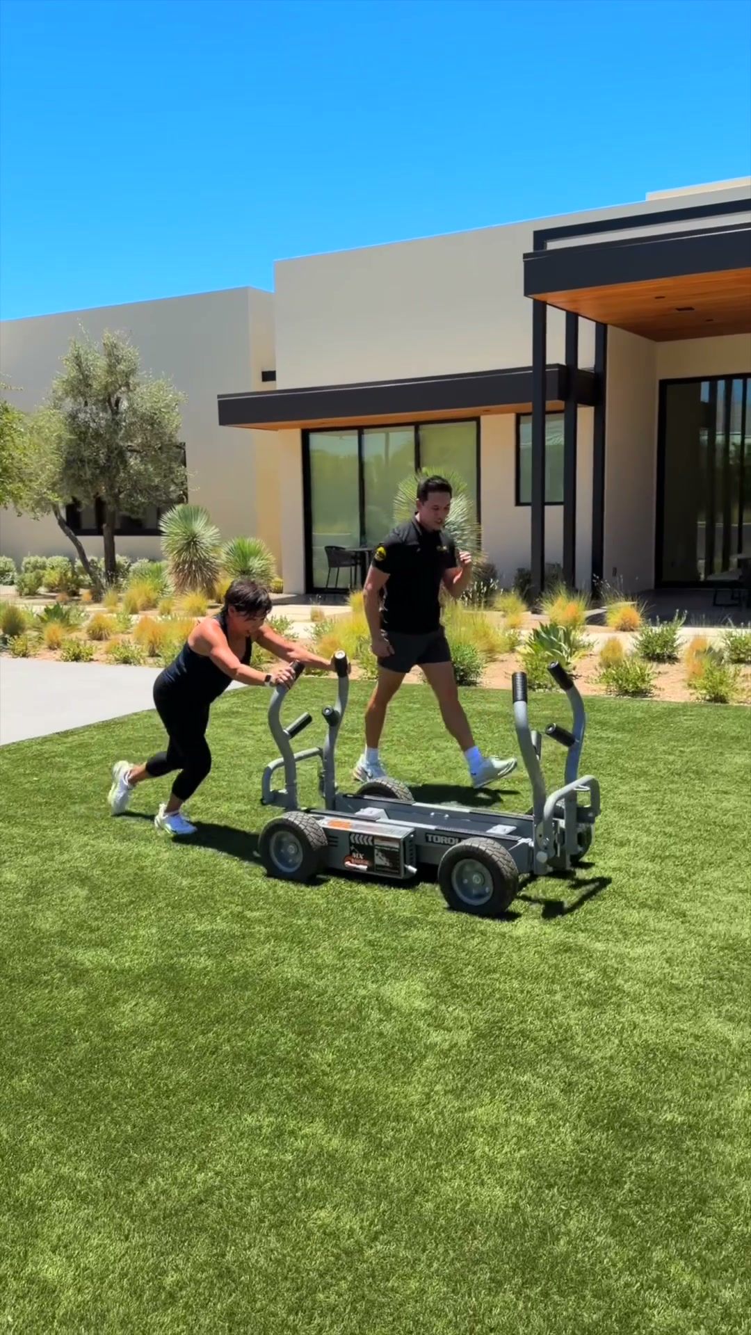 Client pushing a weight sled across a backyard lawn with her trainer