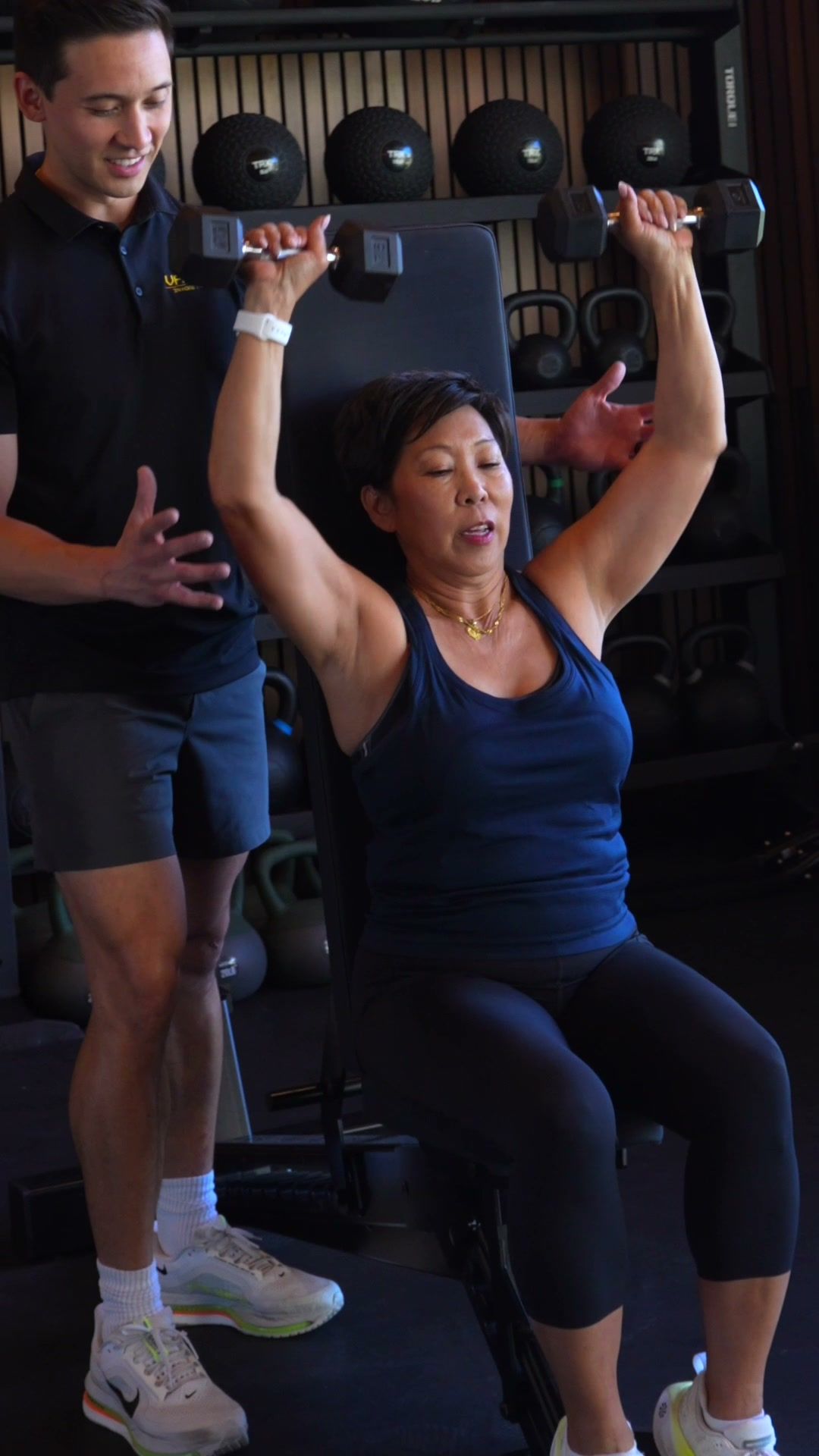 Trainer spotting a client’s overhead dumbbell press